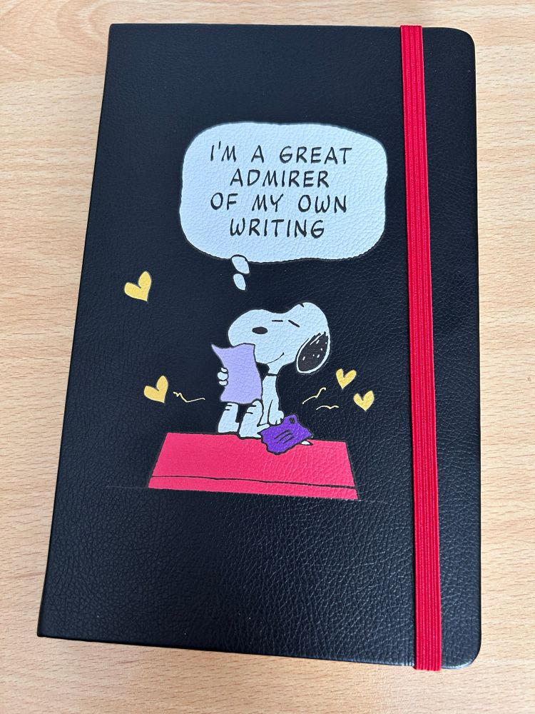 Photo of a Moleskine Snoopy notebook. It has a picture of Snoopy, surrounded by love hearts, holding a piece of paper, and a speech bubble saying "I'm a great admirer of my own writing"