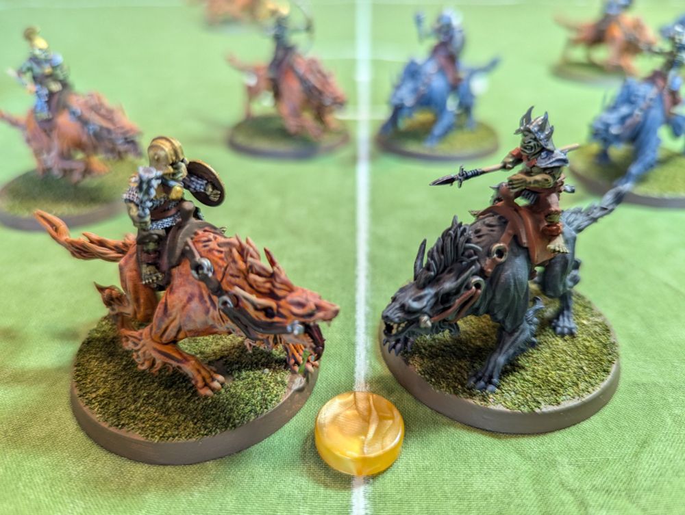 Two teams of painted miniatures of goblins riding on wargs facing off on a football pitch.