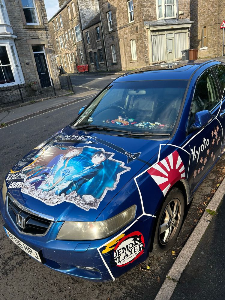 A car parked near my house with lots of inexpertly painted scenes and slogans from Japanese cartoons.