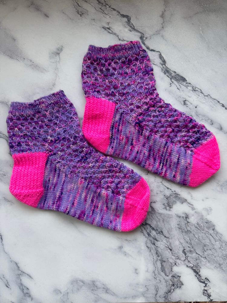 Hand knit socks in pink and purple on a marble surface. 