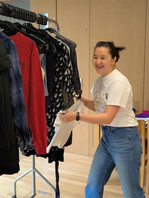Student smiling while sorting clothes at Lincoln College’s Waste Not Want Not swap shop — a student-led sustainability project promoting reuse and circular fashion.