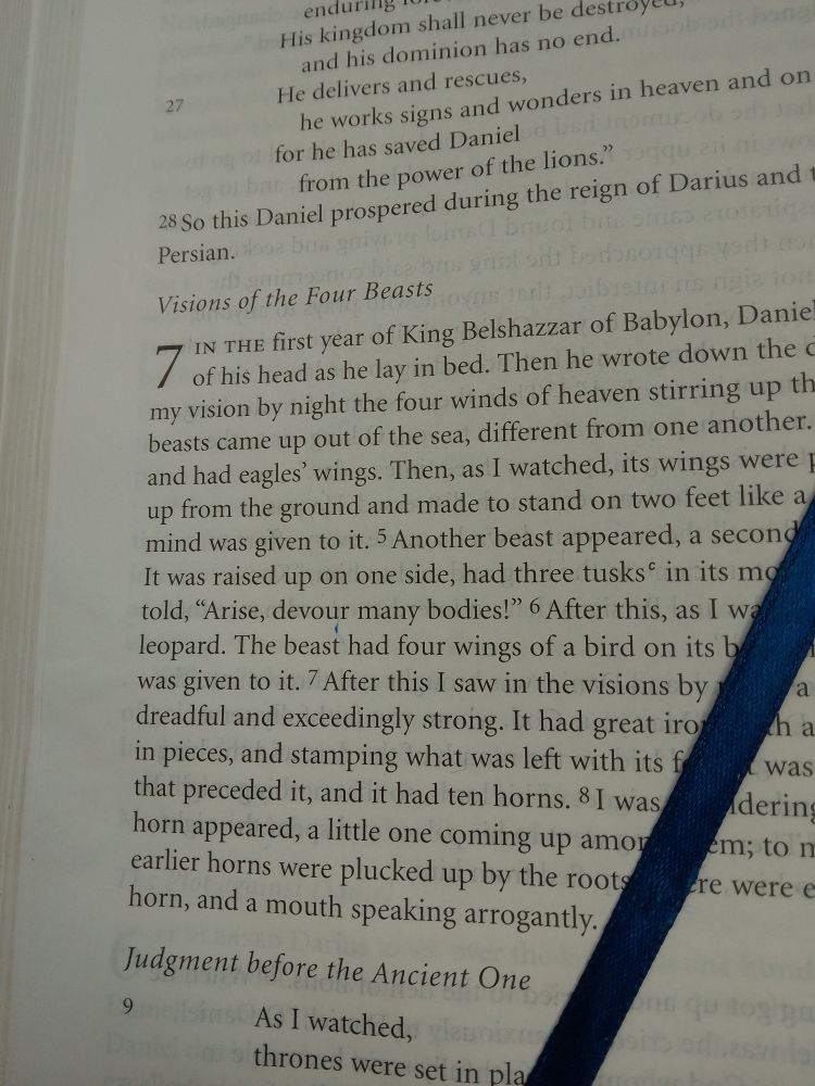 bible open to Daniel chapter 7. thin blue ribbon bookmark is seen over the lower right corner.