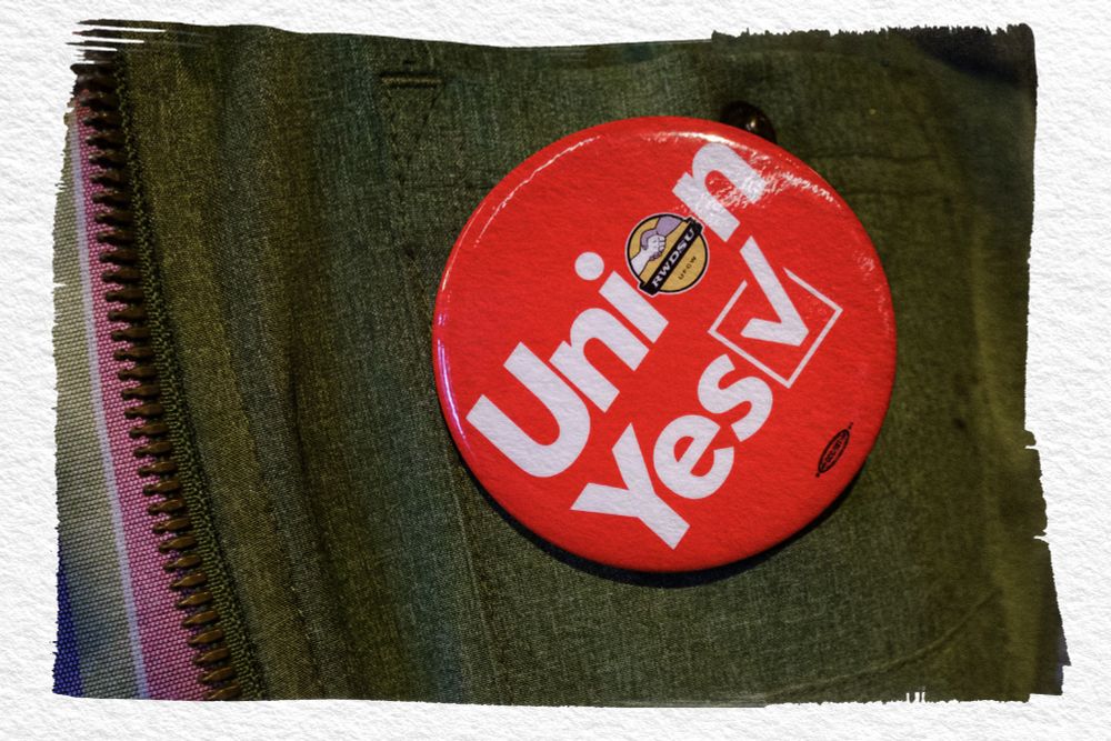 A close-up photograph of a red button that says "Union Yes" on the army green jacket of an REI SoHo worker from March 2022. In small type you can see the logo for RWDSU, the Retail, Wholesale and Department Store Union.