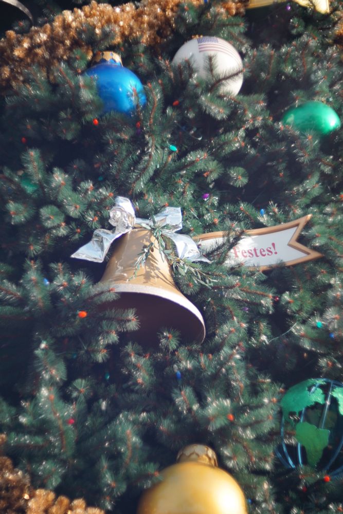 A christmas ornament of a golden bell with a silver bow at the top, and a ribbon