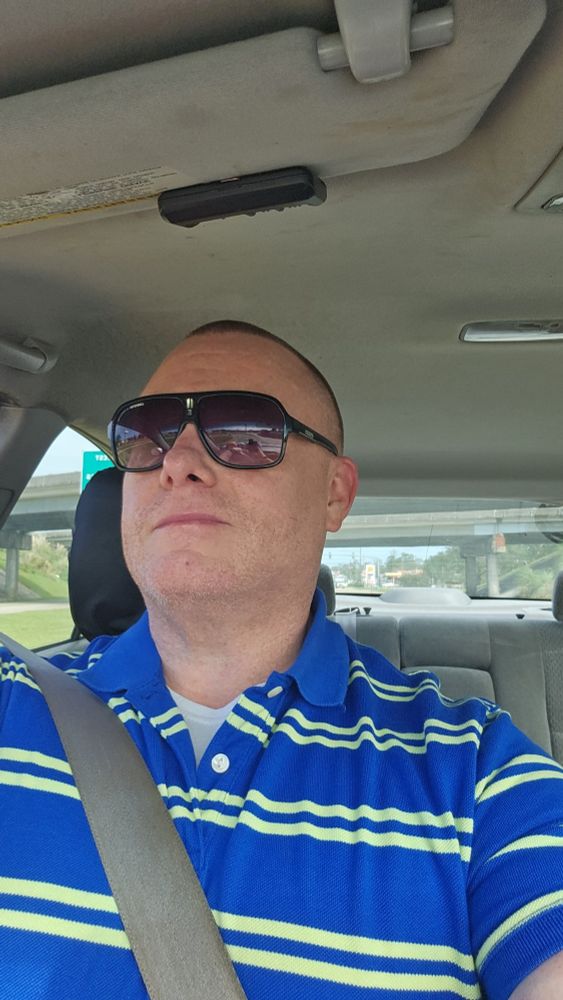 Man with buzz cut red hair, sunglasses, in a blue and high lighter yellow striped polo shirt