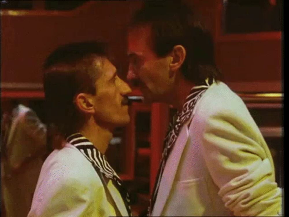 a man in a striped shirt is kissing another man in a white suit