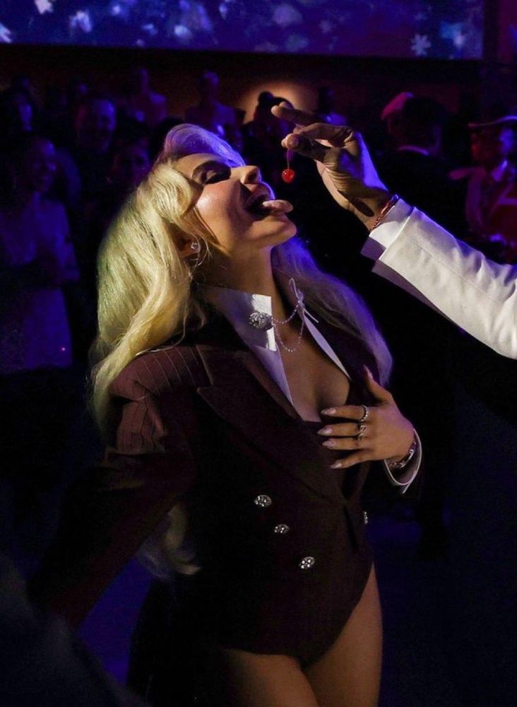 Sabrina at Met gala in brown body suit being fed a cherry 
Her mouth is open and she’s smiling 