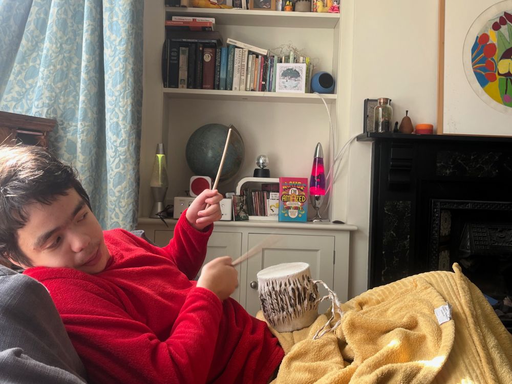 Joe lost in music while listening to Kraftwerk's Autobahn and drumming on a small Kenyan drum. In the background is John Harris's book Maybe I'm amazed next to lava lamp