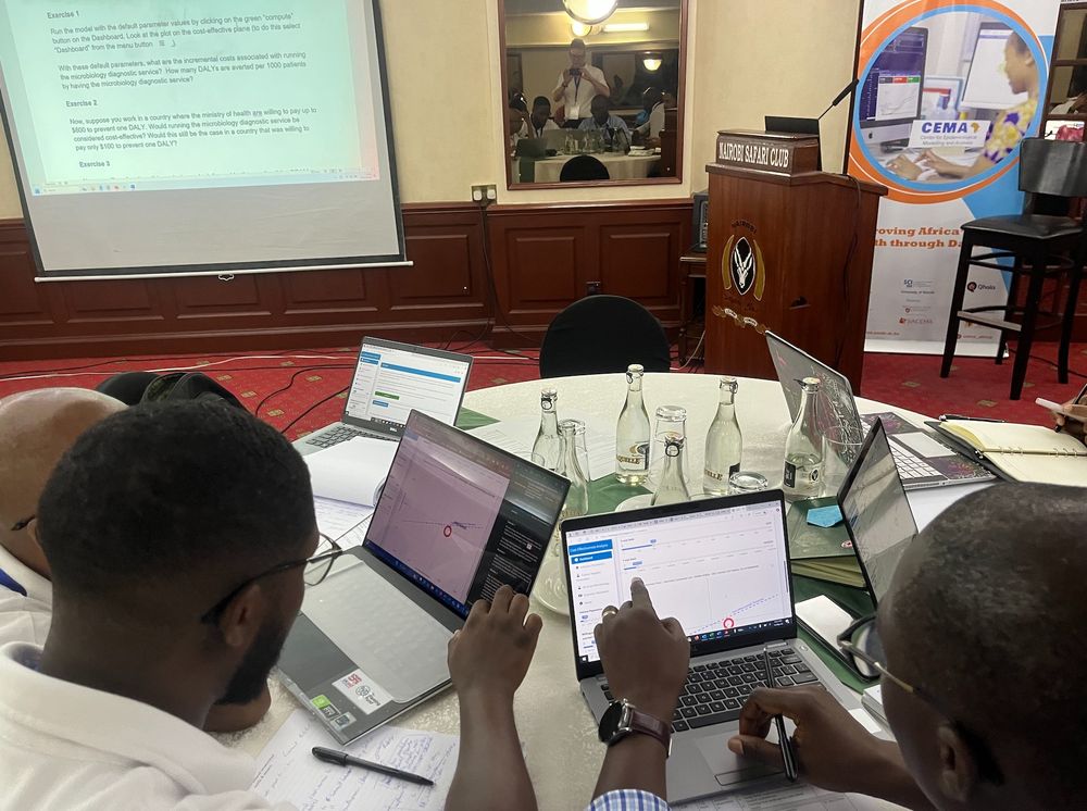 students on short course point at laptop screens which is running an R Shiny web application about cost-effectiveness of maintaining a microbiological diagnostic lab which is based on this paper https://www.medrxiv.org/content/10.1101/2024.05.14.24307355v1