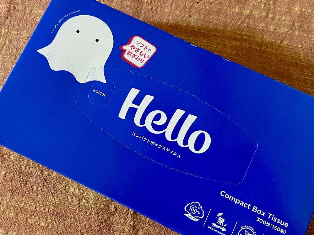 オレンジの布の上に青いティッシュ箱が置いてあり、それを上から撮影している。
箱にはお化けのイラストと中央に「Hello」の文字が書かれている