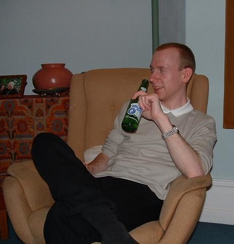 A pic of me in my mid 20s from Xmas 2002. I'm sat in a light brown armchair, and dressed in black jeans and a beige top with the sleeves hoiked up to my elbows. My light brown hair is clipped quite short and I have a very deep widow's peak. I'm holding a bottle or Rolling Rock beer.