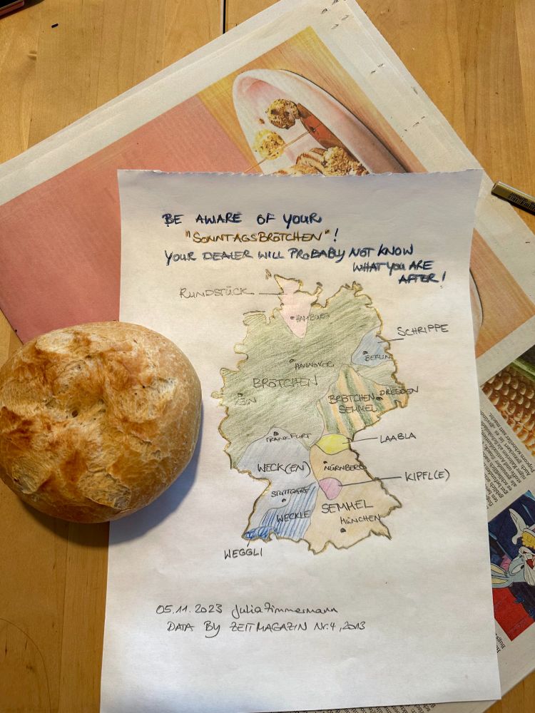 A map of Germany hand-drawn on a piece of paper, showing how bread rolls (Brötchen) are called in different regions, lying upon a newspaper. A bread roll on the left.