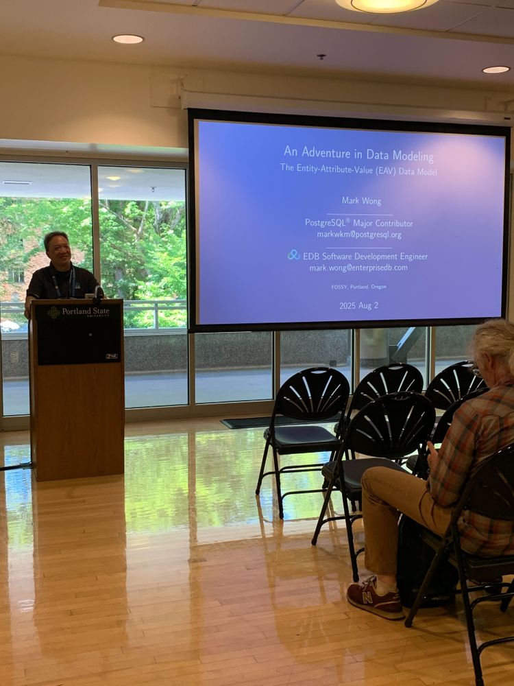 Mark Wong at a speakers desk, next to a screen with a slide up that says "An Adventure in Data Modeling"