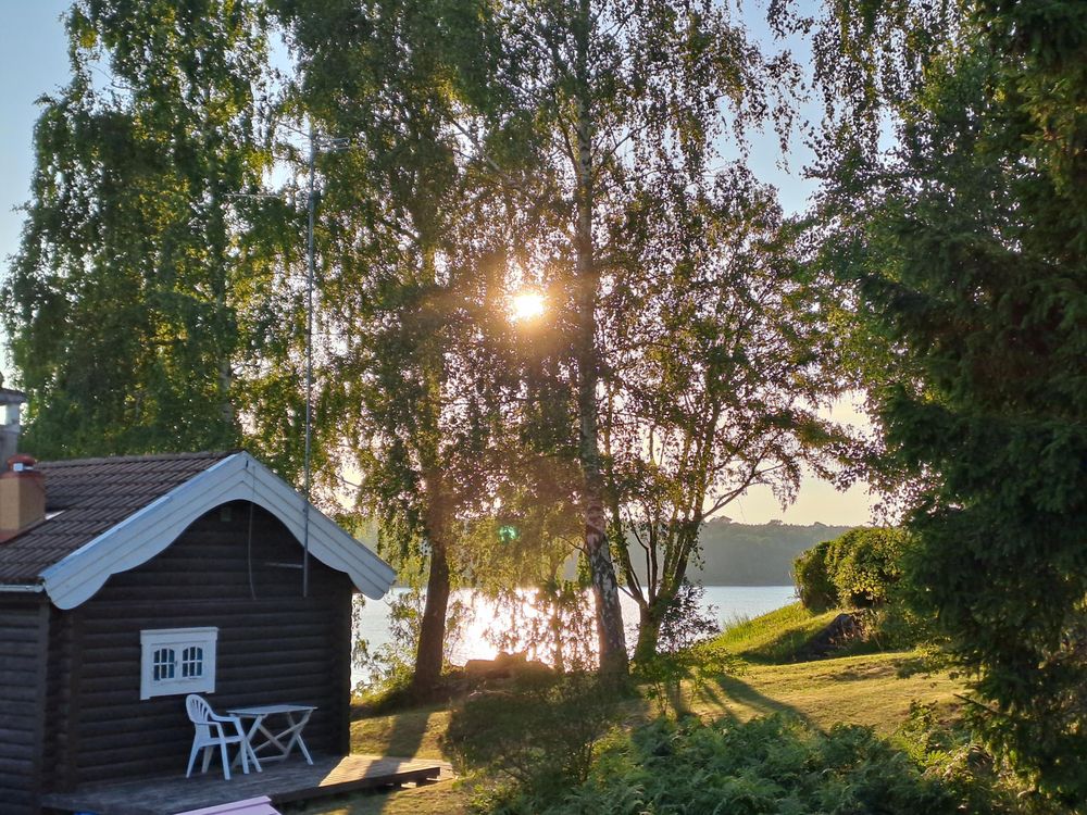 Photo of the Glan lake at sunset, sun shining through trees, red hut in forgetting