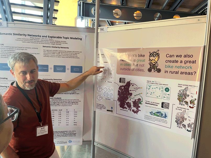 Researcher in red shirt presenting a poster, pointing to it