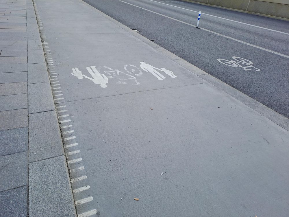 Photo of five lanes. Left for pedestrians. Second also for pedestrians, but was previously a protected bike lane. Third a previous car lane, now a protected bike lane. Fourth the single left car lane. Fifth bus lane. 