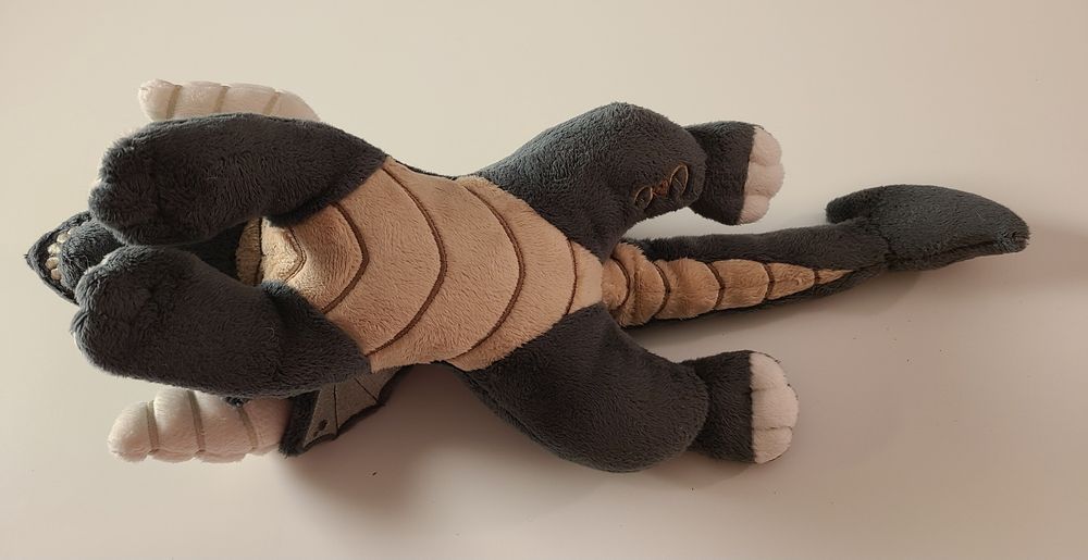 A small, floppy, black dragon plush made by hand. Grey fins, green eyes, cream horns and claws, and skull-like face. Made with soft, minky fabric with embroidered details. Inspired by dungeons and dragons and classic ttrpg games. Filled with light stuffing and polly pellets, the fun textures make this a great plush for fidgeting and stimming.