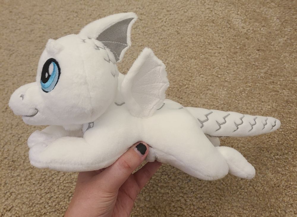 A small, floppy, white dragon plush made by hand. Blue eyes, detailed scales, and two shades of white. Made with soft, minky fabric with embroidered details. Inspired by dungeons and dragons and classic ttrpg games. Filled with light stuffing and polly pellets, the fun textures make this a great plush for fidgeting and stimming. For sale!