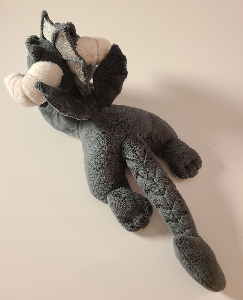 A small, floppy, black dragon plush made by hand. Grey fins, green eyes, cream horns and claws, and skull-like face. Made with soft, minky fabric with embroidered details. Inspired by dungeons and dragons and classic ttrpg games. Filled with light stuffing and polly pellets, the fun textures make this a great plush for fidgeting and stimming.