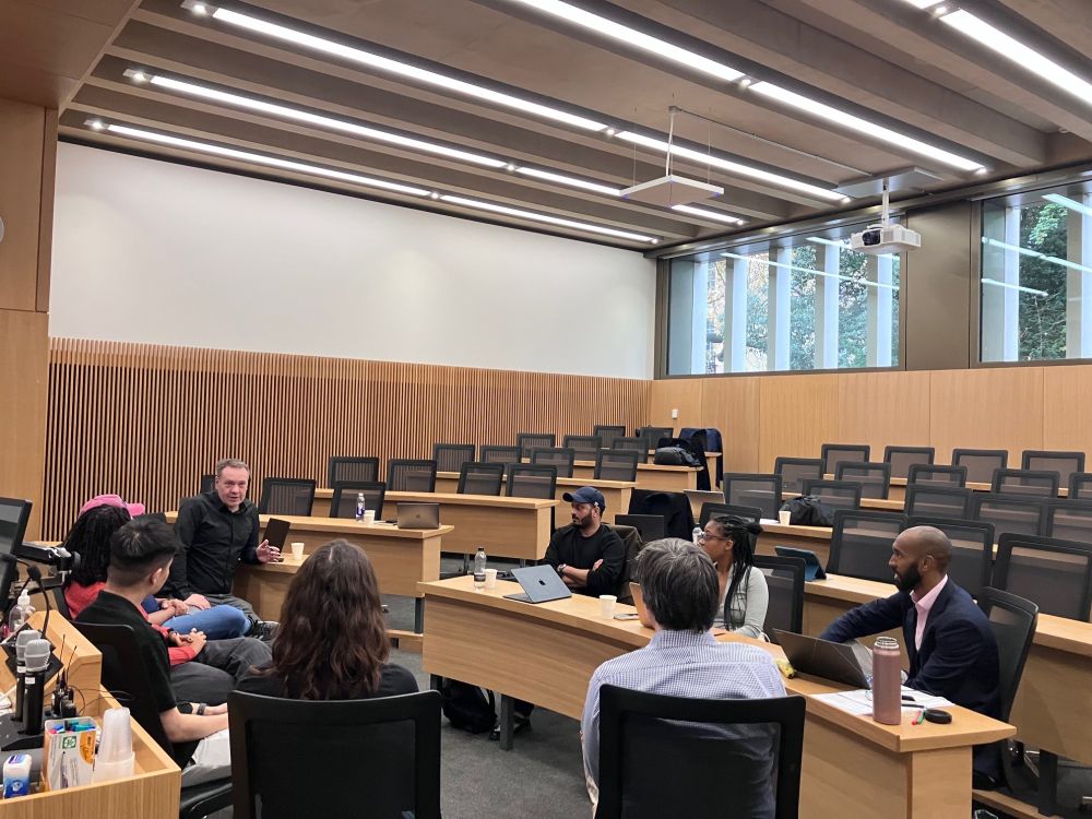 A small group of eight MSt Social Innovation students sit on a circle of chairs in a lecture theatre at Cambridge Judge Business School, taking part in a seminar to help refine their dissertation ideas. 
