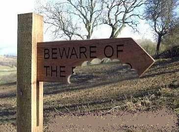 A wooden sign in an outdoor area. It reads "beware of the" and the rest of the sign is missing, as though it has been bitten off. 