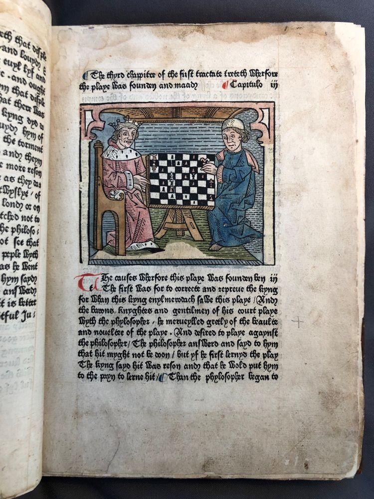 One page from the 1483 edition of The Play of Chess, featuring a hand-coloured woodcut illustration. the illustration depicts two men playing chess.