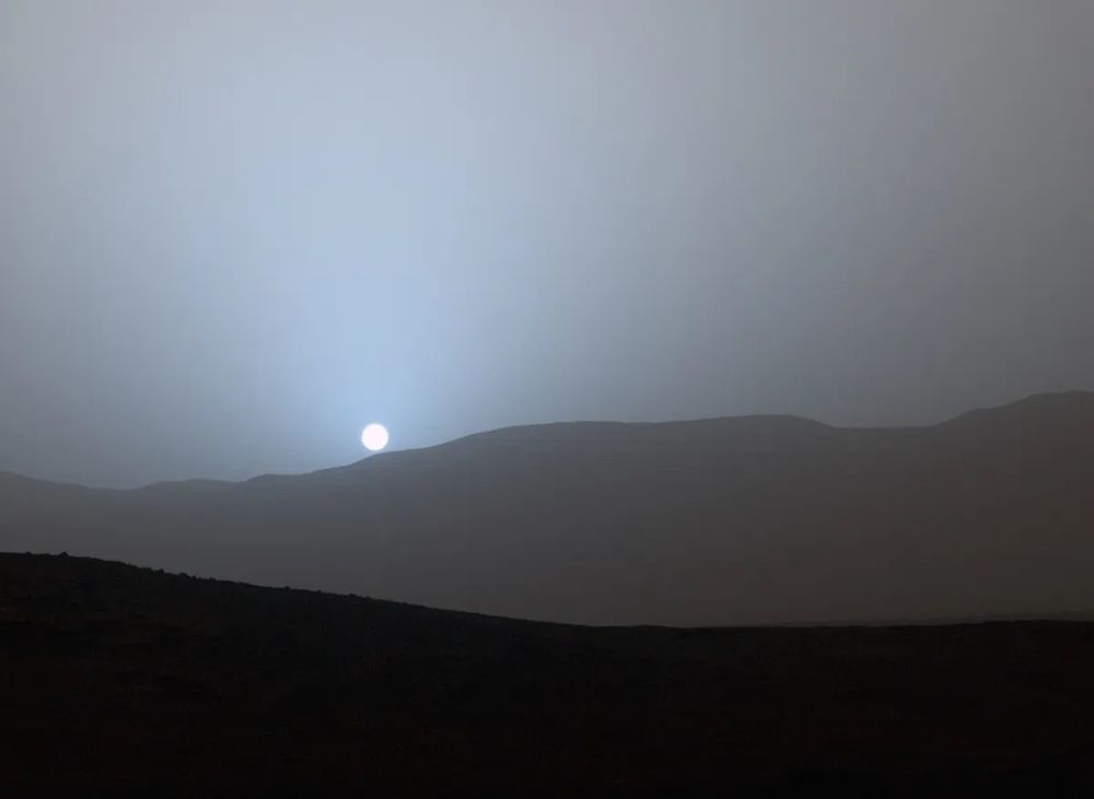 The sun(bluish in colour) sinks below the horizon(of mountains) in this stunning panoramic view captured by NASA's Spirit Mars rover in 2005