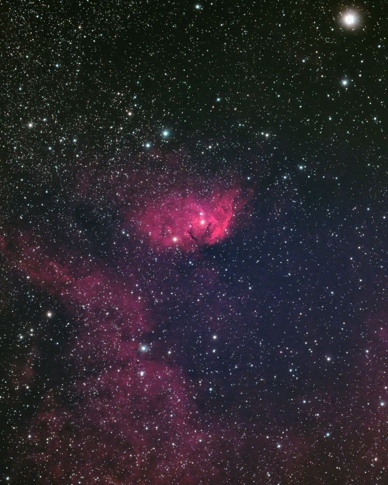 A flower-shaped glowing nebula against a sea of stars. Fainter wisps of nebula surround it.