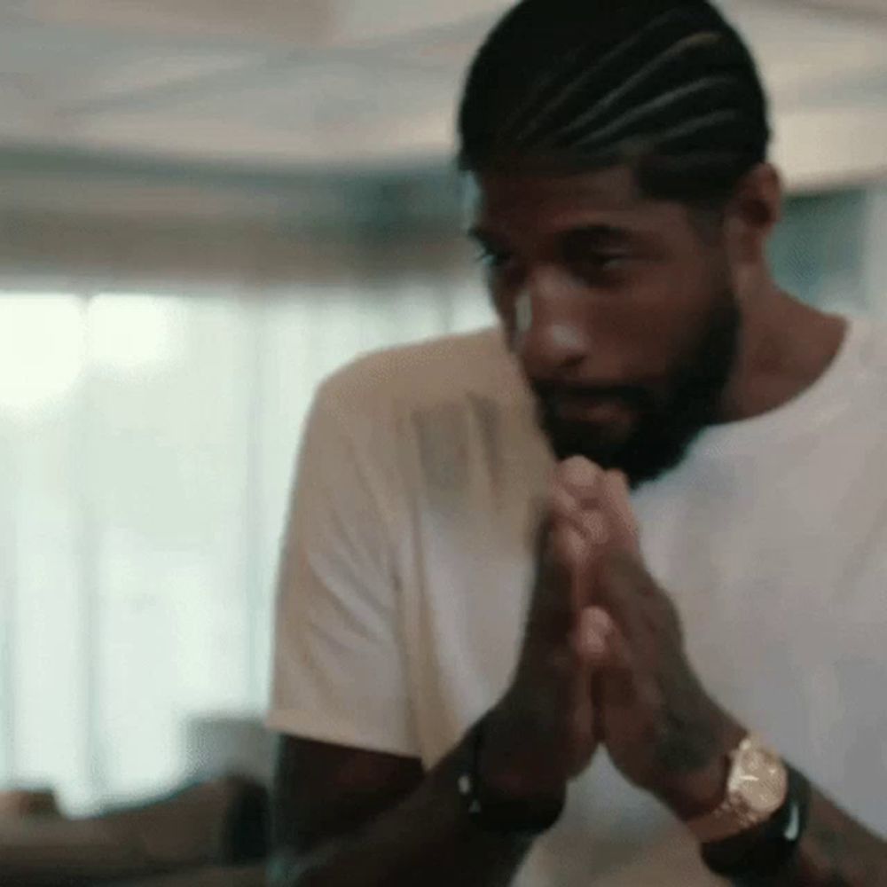 a man with a beard and braids is praying with his hands together in a room .