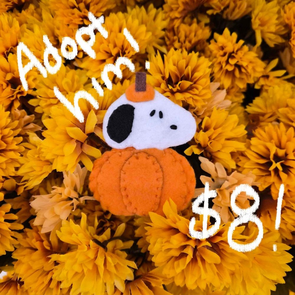 A pumpkin Snoopy keychain handmade from felt and fleece on top of a floral background.