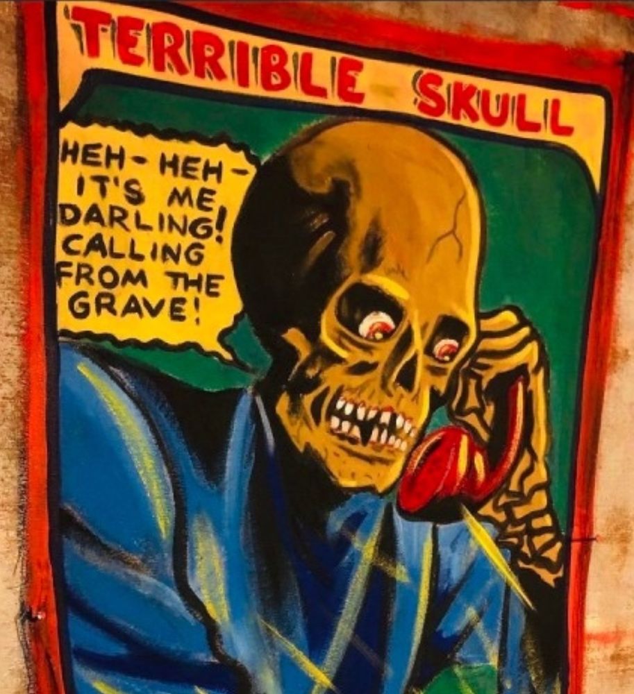 A vividly colored painting of an old-fashioned looking cartoon showing a medium close up of a skeleton clothed in blue and holding a red telephone presumably to its ear hole. Eyeballs are in the sockets and looking downward. At the top are the words TERRIBLE SKULL in red. A word balloon next to the skeleton says “HEH- HEH- IT’S ME DARLING! CALLING FROM THE GRAVE!”