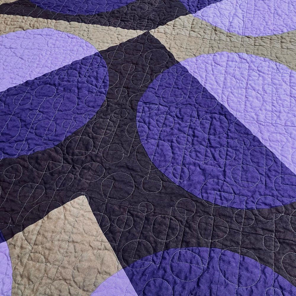 Close up of a purple and brown quilt made of half square triangles with circles inside 