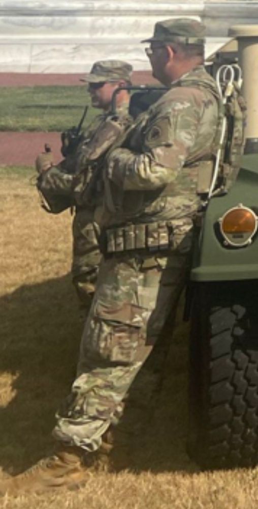 Photo of a guy in fatigues with zip ties on his back and more fucking pouches on his belt than Liefeld’s Cable. But the fella is neither young nor fit. He kind of looks like they press-ganged a retired plumber into leaning against a humvee in a field. 