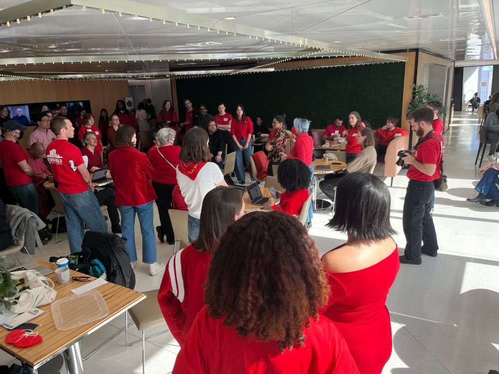 Photo of a crowd of people in red shirts gathering in central office area