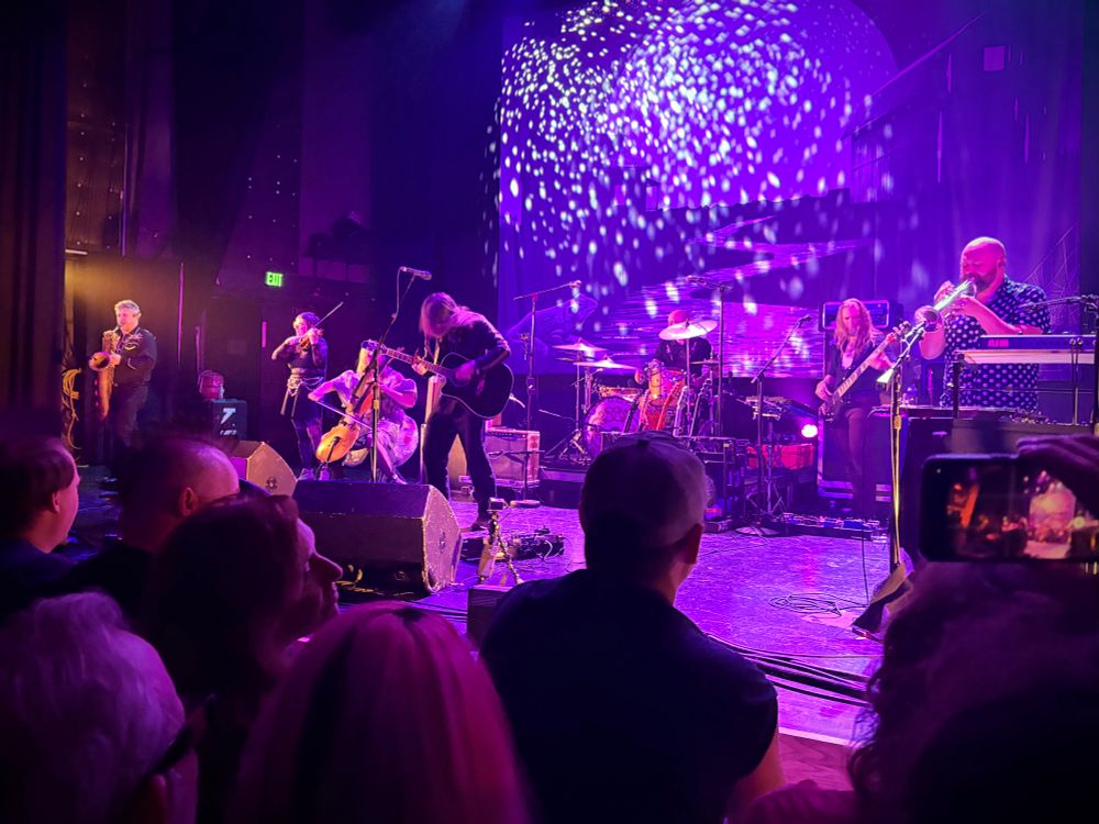 Concert photo taken from the floor. Purple lights illuminate the band. 