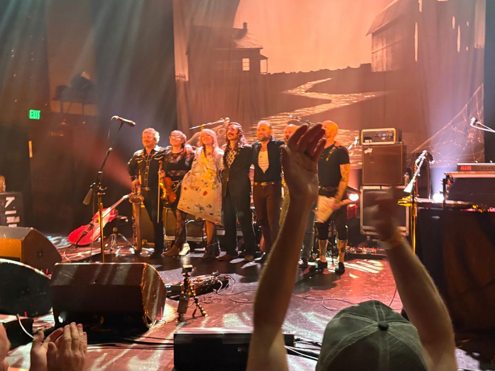 Concert photo taken from the floor. The band gathers on stage preparing to take a bow. 