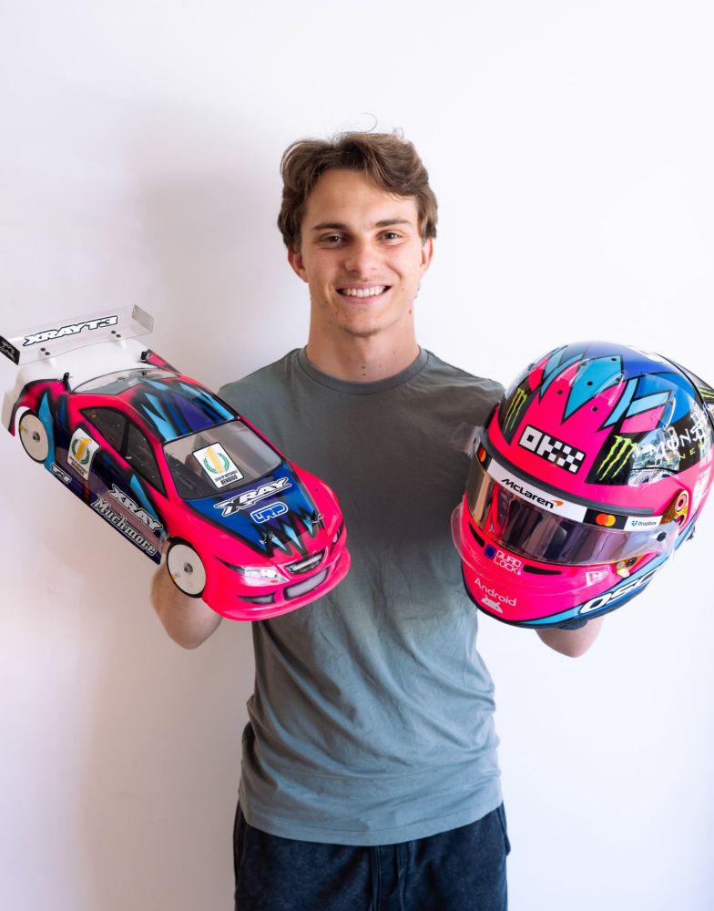 2025 oscar piastri holding his rc and Vegas helmet - it's neon pink, with different shades of blue in a diamond shape on top