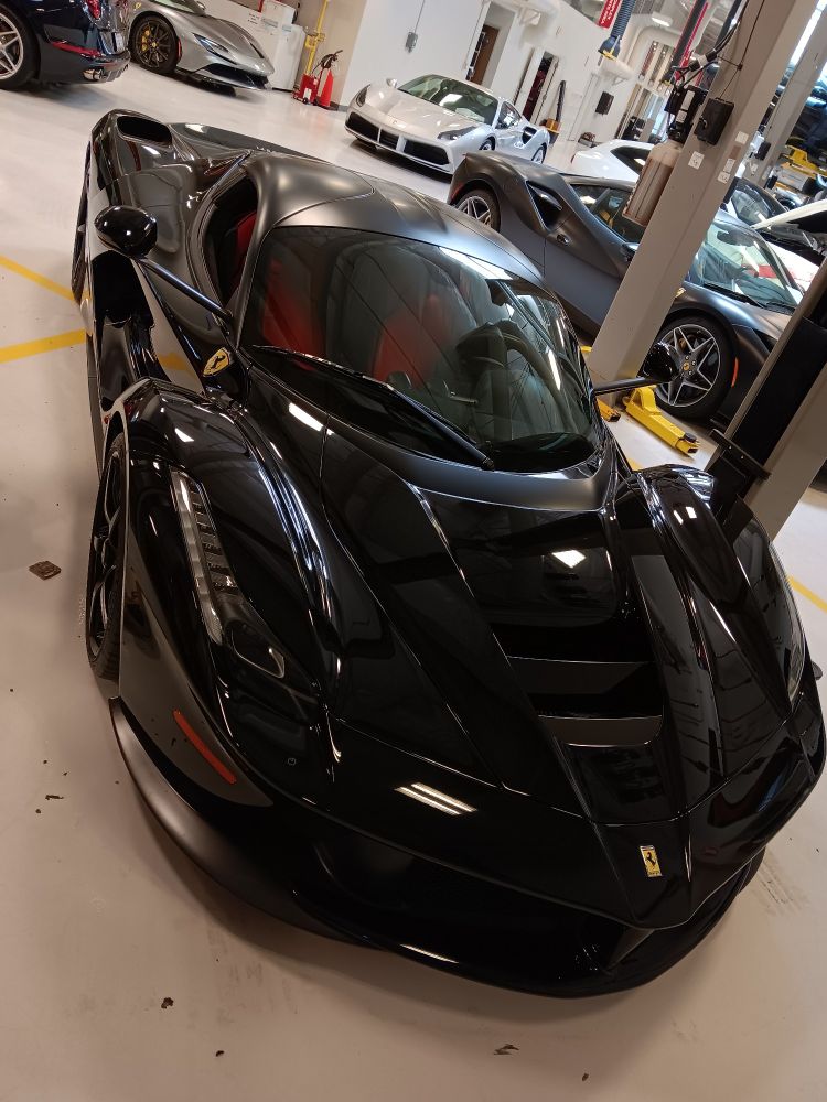 A black 2014 or '15 La Ferrari sits in a repair dock. Other Ferraris can be seen in the background