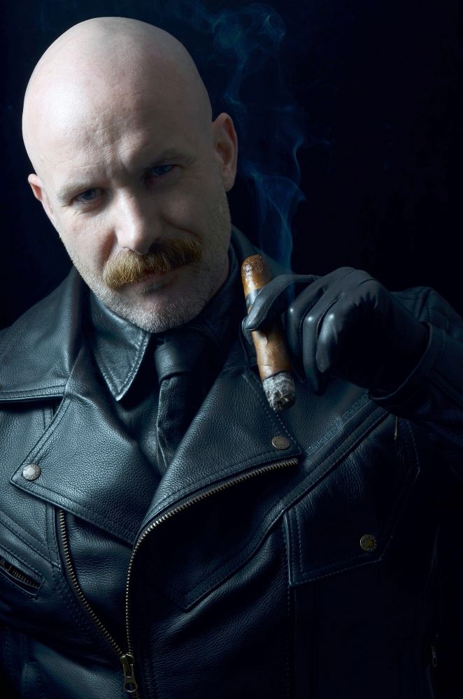Male with shaved head and moustache in full black weather with tight leather gloves on