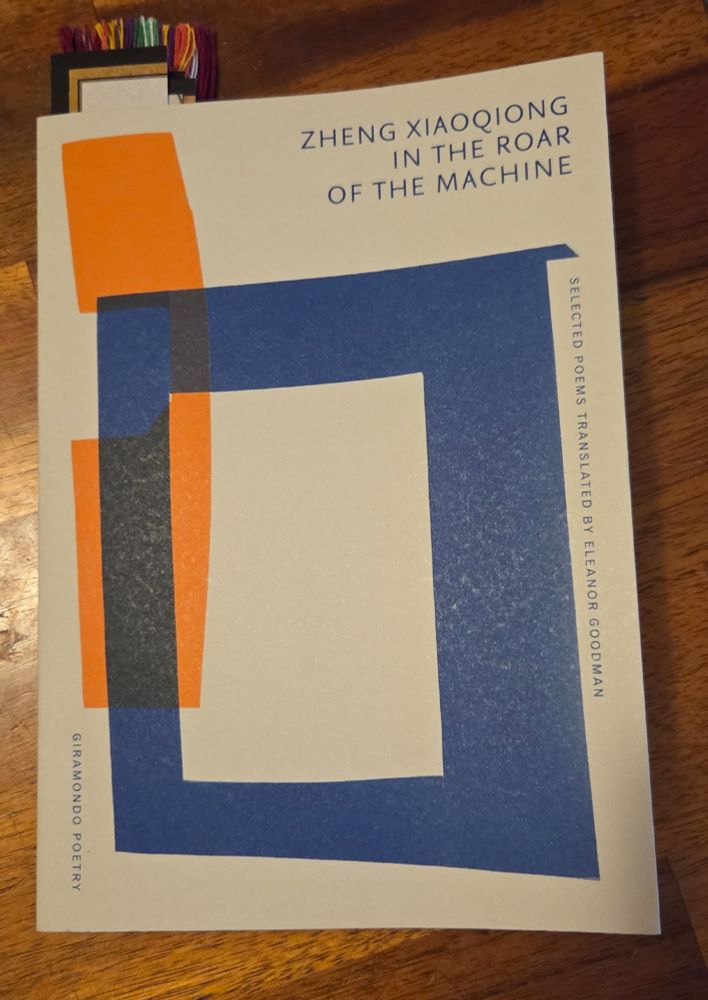 A poetry chapbook: Zheng Xiaoqiong, In the Roar of the Machine, Selected Poems translated by Eleanor Goodman. The cover is off white with a neon orange phone handle shape covered by a large dark blue open square shape. There are several bookmarks in the book.