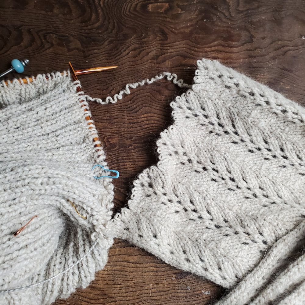 natural color yarn being knit off a lace panel scarf into 2x2 ribbing  on wood background 
#knitting #knitsky 🧶