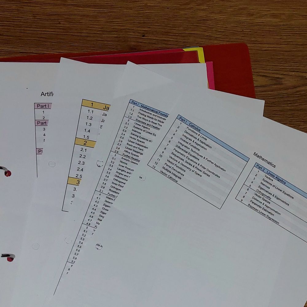 Loose pages with tables listing topics for maths and coding with bright headings on a wooden table
