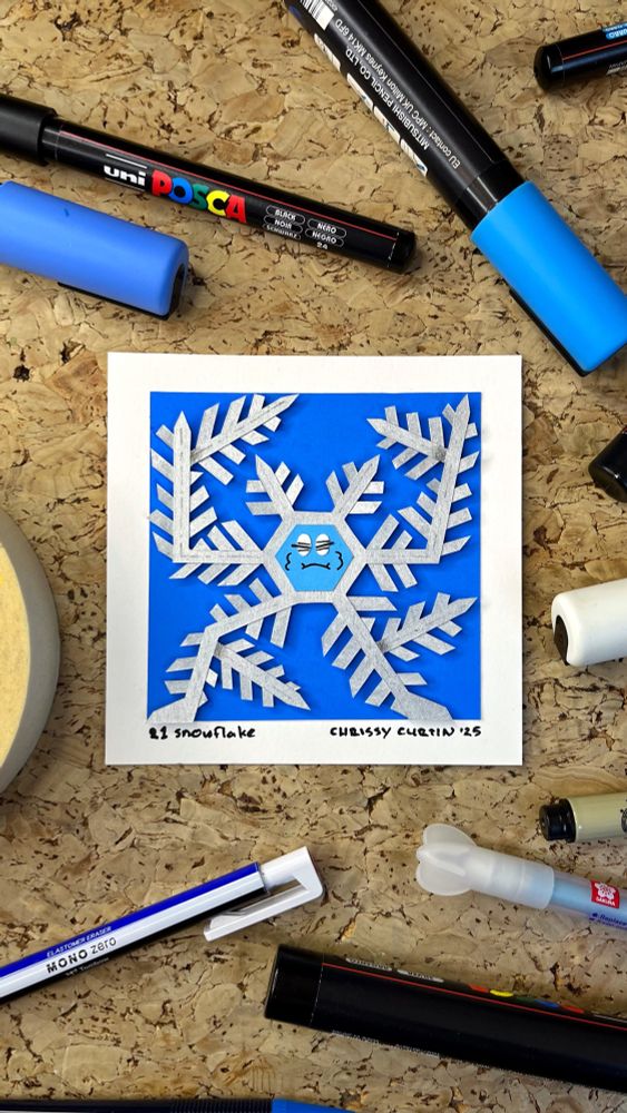 Photo of my paper cut illustration of a cute snowflake with a silly face.