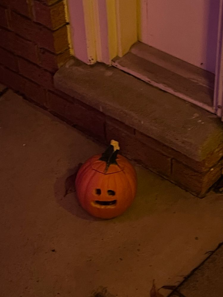 Tiny tiny jack o lantern on a stoop in front of a house 