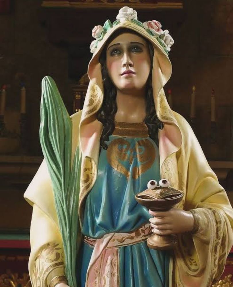 imagem de santa luzia segurando um cálice com dois olhos numa almofada que parece um fantoche 