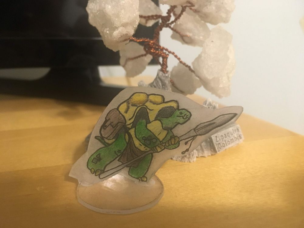 A bipedal tortoise with a bag at his hip and a loincloth. He stands ready to fight with a spear in his hands