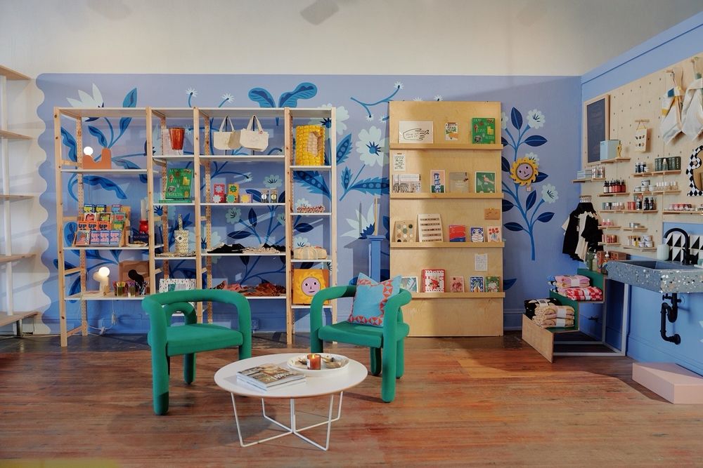 The inside of duets store. The walls are lined with shelves of products. In front are two cool green chairs and a coffee table