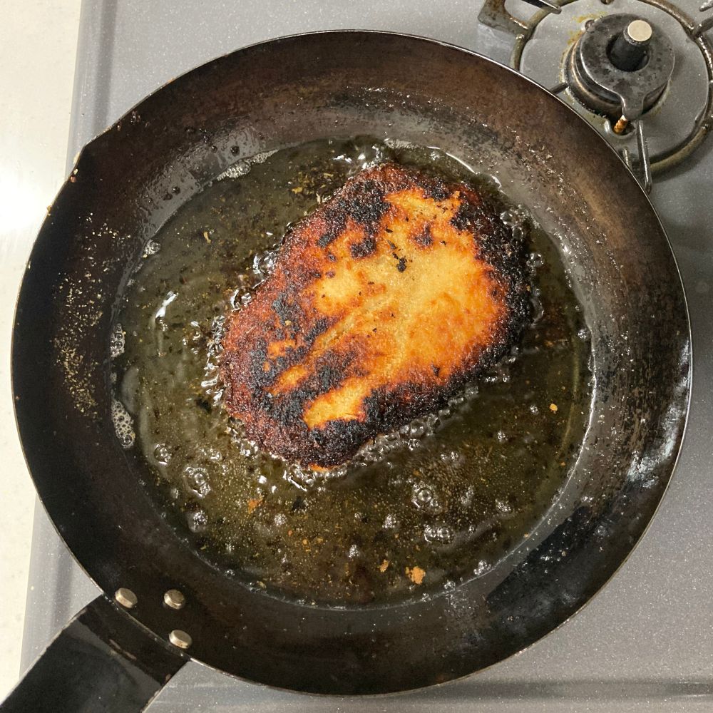 パン粉をつけ、フライパンで揚げ焼きにしている鶏胸肉。パン粉が黒く焦げている。