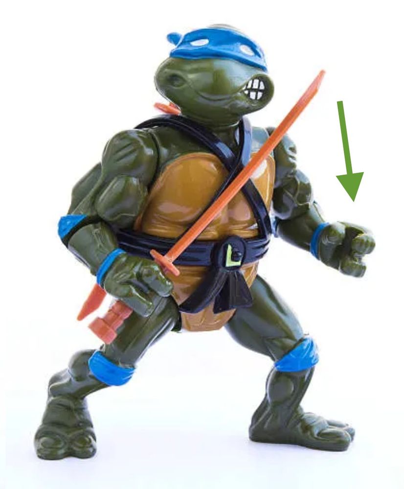 Photo of a 90s Teenage Mutant Ninja Turtles figurine. There is an arrow pointing at the hand to suggest the fuse on the other photo would fit there.
