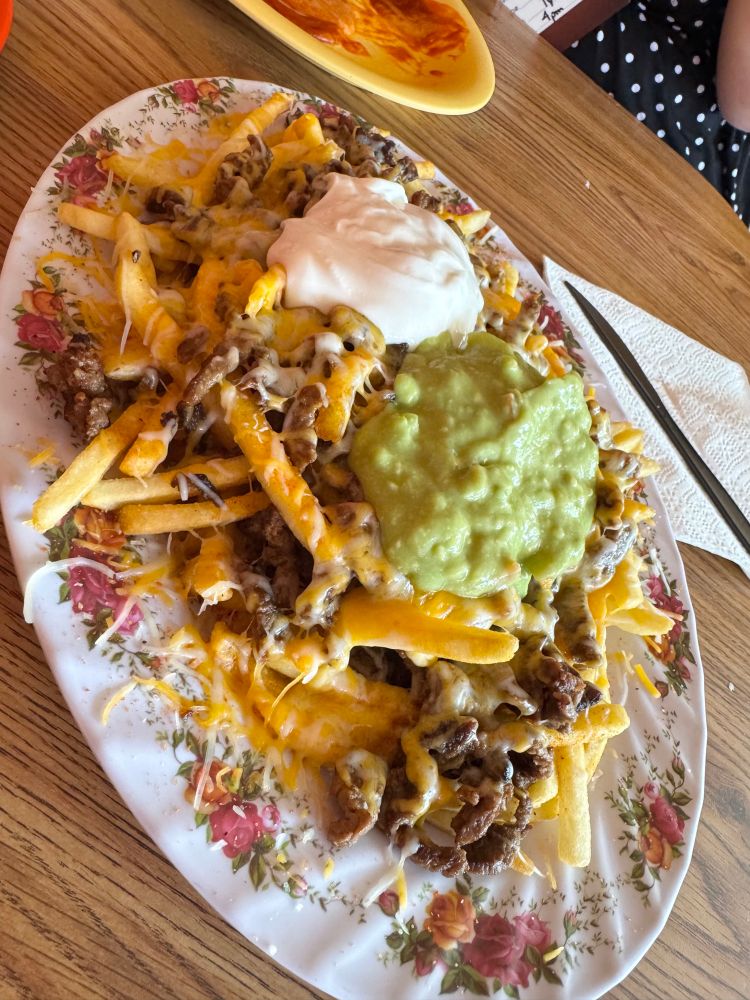 A plate piled high with French fries covered in steak cheese sour cream and guacamole 